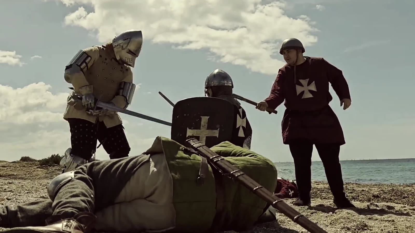 Fotograma d'un curtmetratge: tres cavallers amb cota de malla i escut templer a la vora del mar.