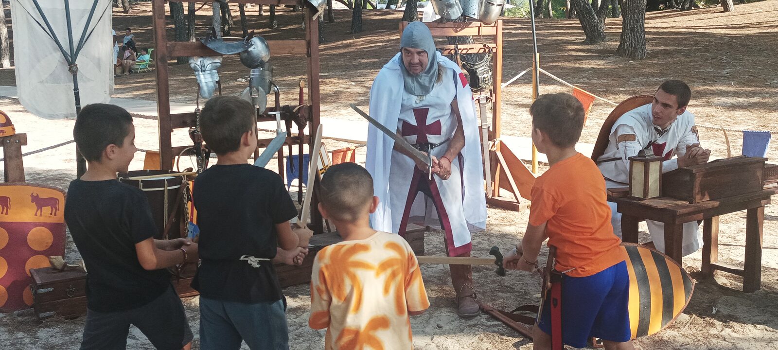 Un recreador amb sobrevesta de creu roja ensenyant el maneig de l'espasa a un grup d'infants al campament de Santa Ponça.