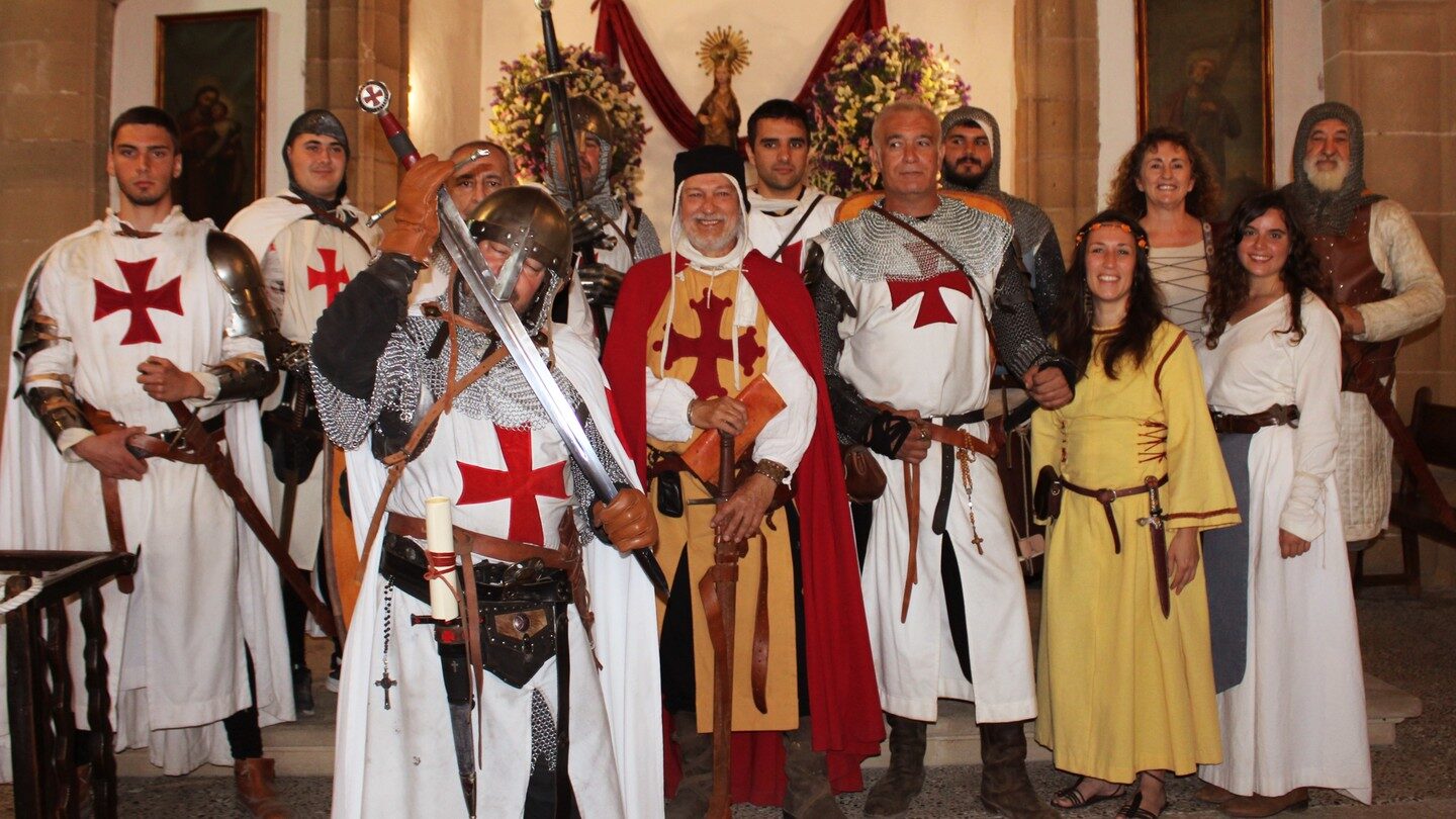 Foto de grup dins una església: recreadors amb cotes de malla, sobrevestes blanques amb creu templera i vestits llargs.